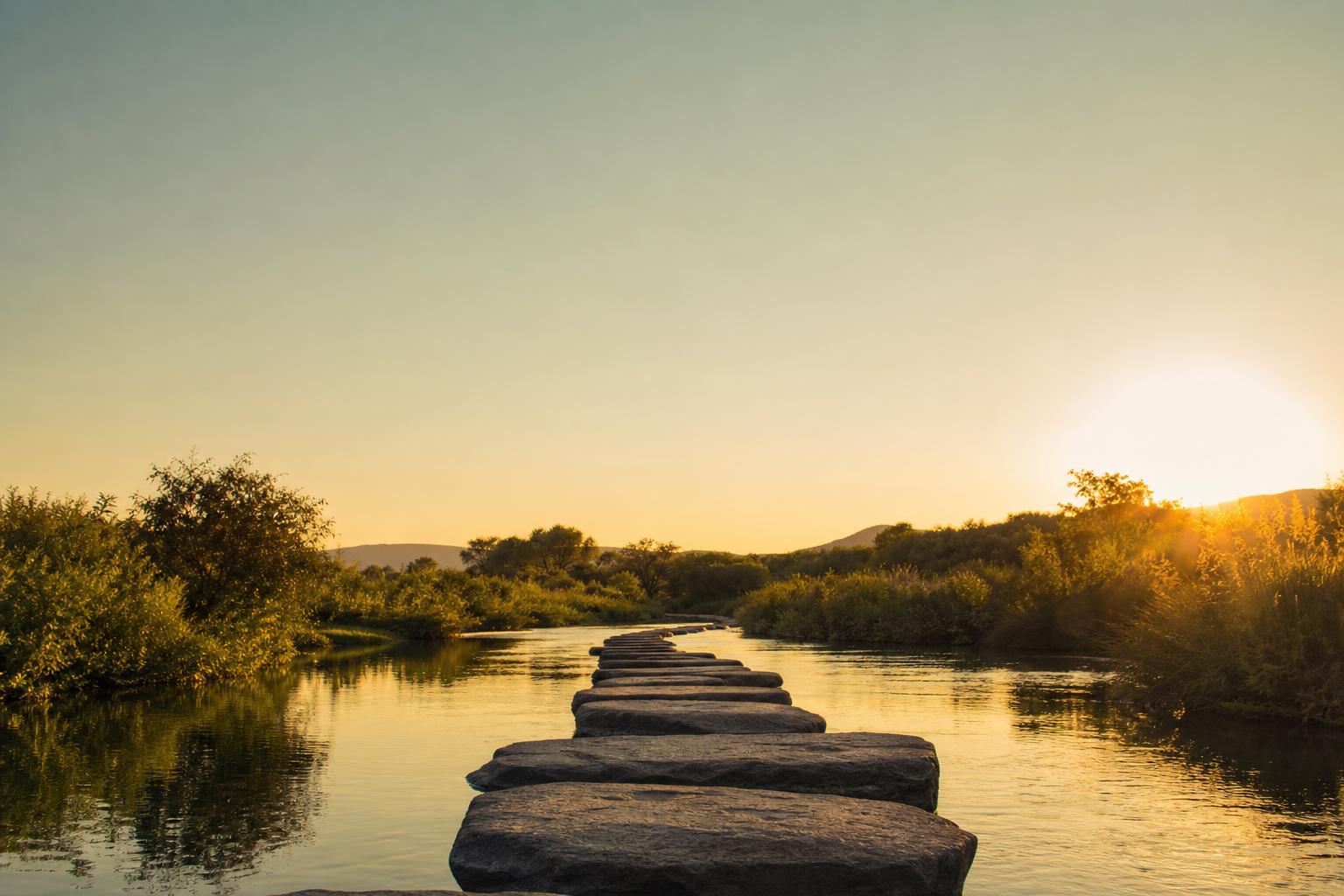 Piedras de paso cruzando un arroyo en calma al atardecer, metáfora de una rutina repetible paso a paso